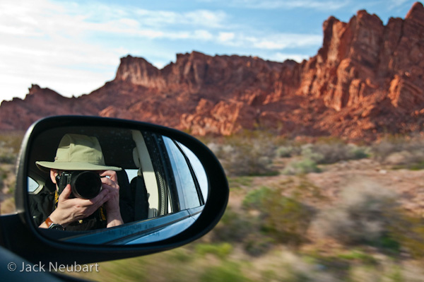 SELF-PORTRAIT. While in the passenger seat on a drive through Valley of Fire, I took this opportunity to focus the lens on my reflection in the mirror, with a wide enough focal length setting (34mm/51mm equivalent) to capture the surrounding desert scenery. Vibration Reduction was apparently at work to prevent camera shake. Photo Copyright  ©2009 Jack Neubart. All rights reserved.