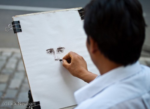 Sketch Artist. I didn't want to disturb this sketch artist as he was working on a portrait; so I avoided flash and shot wide open for a 1/125 sec exposure under open shade. That was sufficient to prevent the artist's hand from blurring, while focusing attention on his work (ISO 100). Copyright  ©2009 Jack Neubart. All rights reserved.